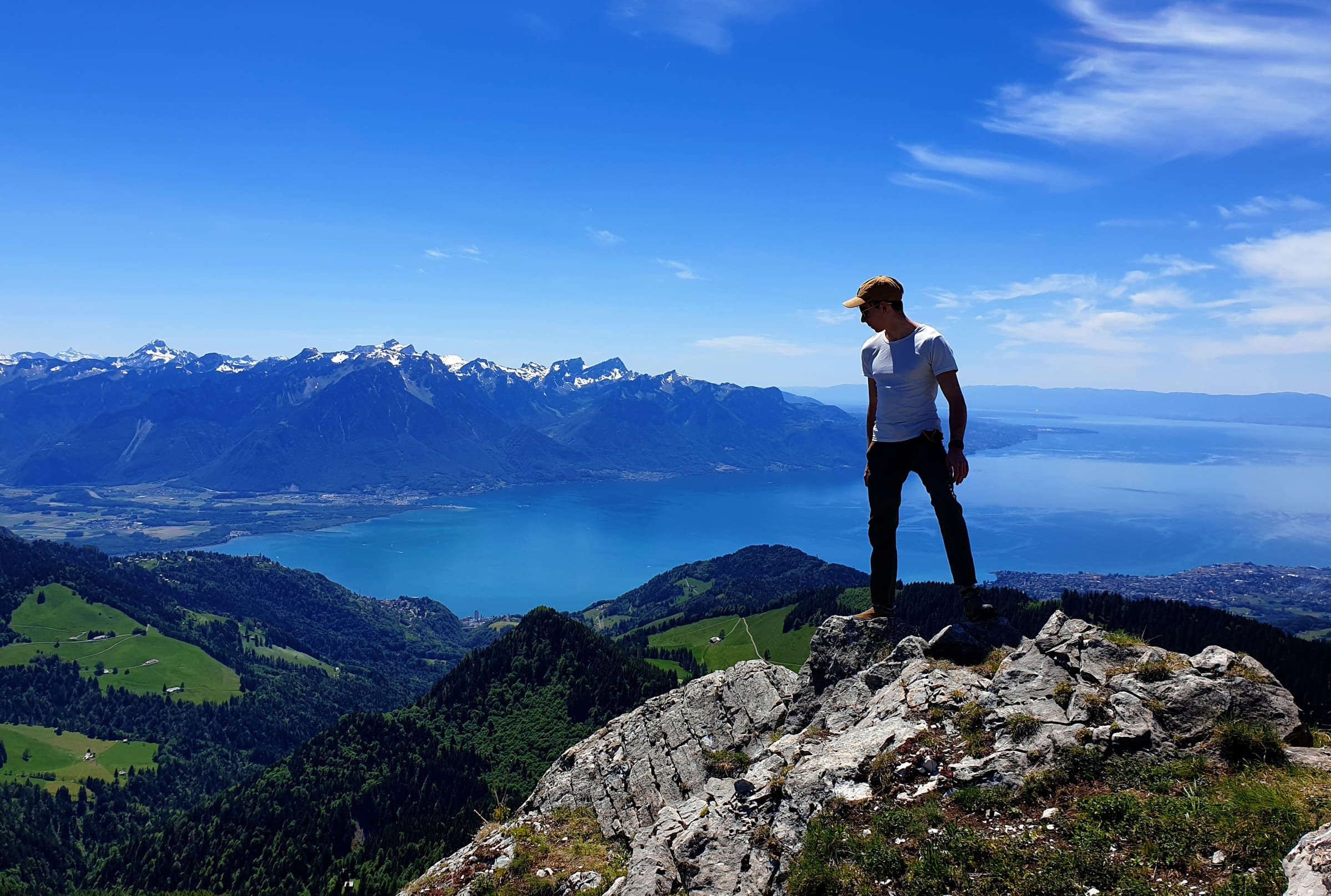 Damien standing on a rock at the top of a mountain, Lake Geneva and the Alps below